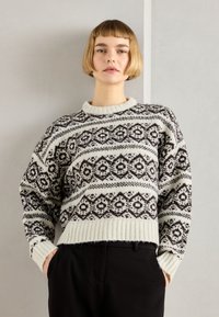 Maglione a maglia con corpo crema e motivi geometrici marrone scuro. Presenta un collo e un orlo a coste, con spalle cadute per una vestibilità rilassata.