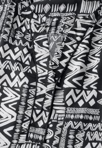 Tissu noir avec des motifs géométriques et en zigzag blancs, avec un décolleté en V et des accents multitechniques, mettant en valeur un design audacieux.