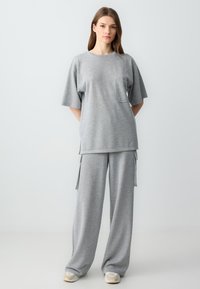 Graues, lässig geschnittenes T-Shirt mit kurzen Ärmeln und Brusttasche, kombiniert mit passenden, weit geschnittenen Hosen mit Seitentaschen und einer glatten Textur.
