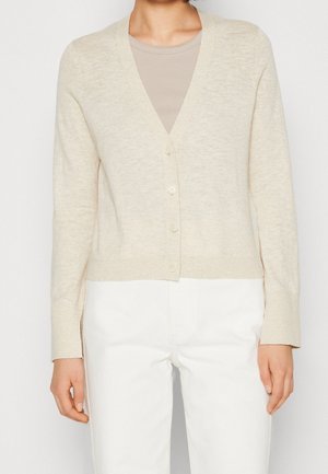 Cardigan leggero beige con scollo a V, sette bottoni e maniche lunghe. Caratterizzato da orlo e polsini a coste, indossato sopra una camicia beige.