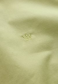 Hele-roheline kangas väikese, sobiva rohelise niidiga tikitud krooni sümboliga, mis on paigutatud keskele.