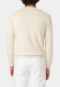 Lichtbeige gebreide trui met lange mouwen, geribbelde kraag en zoom. Gedragen met witte jeans, die een gladde textuur en een aansluitende vorm tonen.