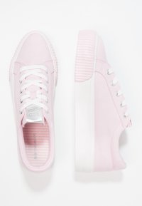 Różowe tenisówki na płótnie z białymi sznurowadłami i teksturowaną gumową podeszwą z pionowymi rowkami. Srebrny akcent na języku.