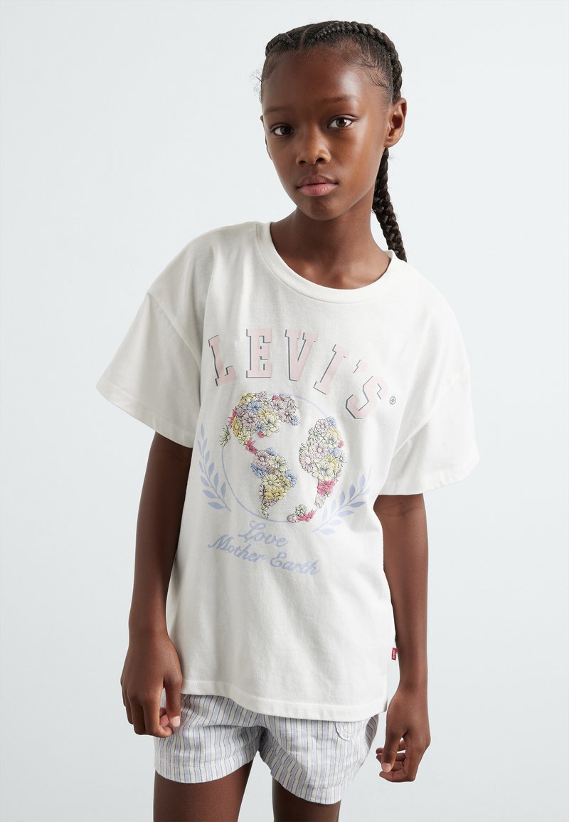 Camiseta blanca de algodón con mangas cortas, que presenta un gráfico colorido de un globo floral y el texto "AMA A MADRE TIERRA", combinada con pantalones cortos a rayas.