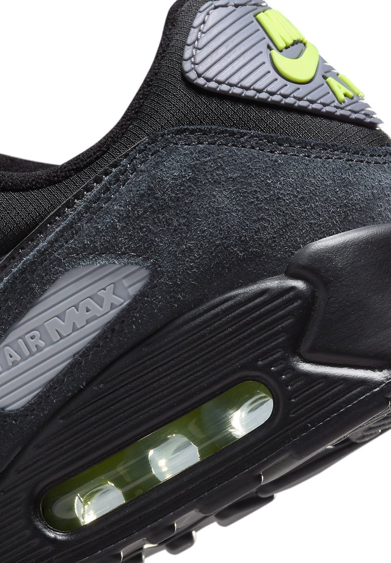 Primer plano del talón de una zapatilla Nike Air Max negra, con una almohadilla de aire visible y materiales de gamuza y goma texturizados.