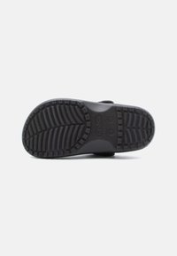 Black rubber sole of a Crocs clog showing textured tread pattern and size markings on a white background.