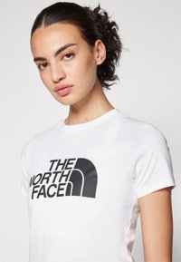 Hvid crew neck t-shirt med et fremtrædende sort logo, der står "THE NORTH FACE." Lavet af glat stof med korte ærmer.