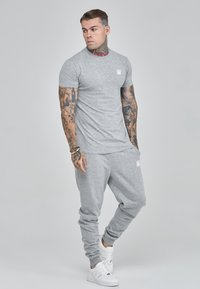 Grijze katoenen t-shirt en bijpassende joggers, met een klein wit logo op de borst en elastische manchetten, gecombineerd met witte sneakers.