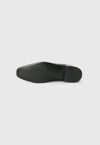 Suela de zapato negro con un acabado texturizado, bordes curvados y tacón reforzado. Diseño plano sin patrones o acentos visibles.