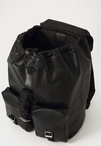 Sac à dos en cuir noir avec un système de fermeture à cordon, deux poches avant et des boucles en métal. Texture lisse avec une forme structurée.