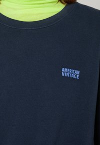 Tumedas sinine särk pehmest kangast ümmarguse kaeluse ja soonikuga kraega. Rinnas on väikene helesinine logo "AMERICAN VINTAGE".