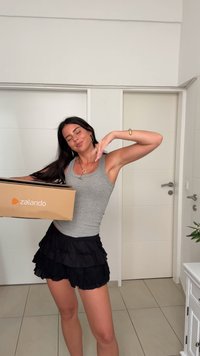 Zalando cardboard box in hand, model wears a grey tank top and a black layered ruffled skirt, showcasing a light and airy design.