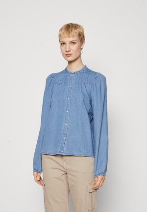 Lyseblå denimskjorte med rund krage, knappelukking foran, pintuck-detaljer på brystet og elastiske mansjetter.