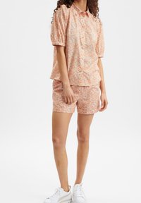 Set composto da blusa a maniche corte e pantaloni corti abbinati in tonalità di arancione e rosa pastello, con chiusura a bottone e fit morbido.