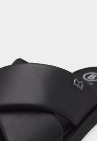 Sandale noire à enfiler avec de larges brides rembourrées qui se croisent sur le pied et un petit logo métallique "B" sur la bride latérale.