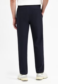 Marineblauwe broek met een rechte pasvorm, twee achterzakken en een soepele stoftextuur, gecombineerd met witte sneakers.