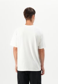 White cotton t-shirt with short sleeves, round neck, relaxed fit, minimal seams, and a small label at the bottom hem.