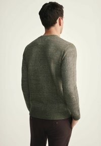 Zielony sweter z dzianiny o teksturowym wykończeniu, z okrągłym dekoltem i ściągaczami. Projekt charakteryzuje się dopasowanym krojem oraz jednolitym kolorem z subtelnymi wariacjami.