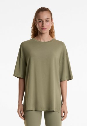 T-shirt ample vert olive en tissu doux, avec un col rond, des épaules dénudées et des manches courtes. Aucun motif notable.