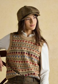 Pleteni telovnik z večbarvnimi cvetličnimi in živalskimi vzorci, bež osnovo, nošen čez belo srajco z ovratnikom, v kombinaciji s rjavim karo klobukom.