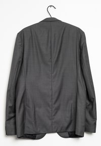 Chaqueta de traje gris colgada en una percha. Presenta un sutil patrón de cuadros, solapas estructuradas y dos aberturas traseras en el dobladillo.