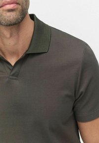 Mörkgrå polo skjorta med en texturerad tyg, en klassisk krage och korta ärmar, med synlig sömdetalj nära kragen.