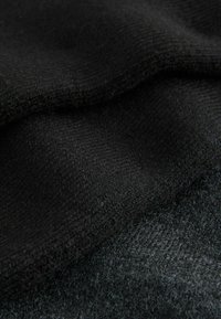 Tela negra texturizada con una apariencia de punto suave, superpuesta sobre un material gris más oscuro, mostrando diferentes tramas y grosores.