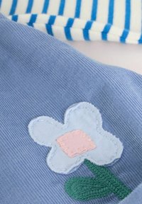 Tissu bleu avec un appliqué d'une fleur blanche au centre rose et une tige verte, à côté d'un tissu blanc avec des rayures bleues.