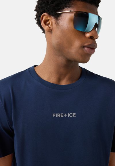 Homme portant des lunettes de soleil bleues miroitées et un T-shirt bleu marine avec l'inscription "FIRE+ICE" en blanc sur la poitrine.