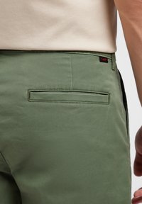 Gröna bomullsshorts med en bakficka och en liten svart logotagg. Slät textur med en skräddarsydd passform.