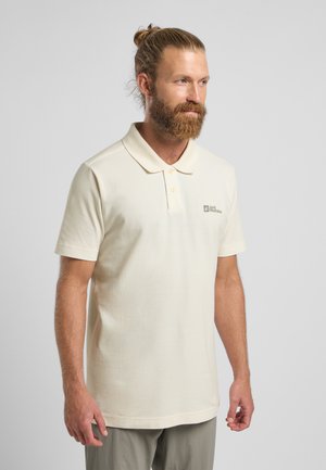 Polo beige en tissu doux, avec un col classique, des manches courtes et un logo subtil sur le côté gauche.