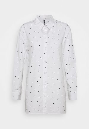Chemise blanche à manches longues avec boutons et col, présentant un motif de petits pois noirs uniformément espacés sur le tissu.