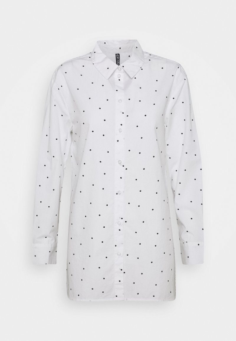 Chemise blanche à manches longues avec boutons et col, présentant un motif de petits pois noirs uniformément espacés sur le tissu.