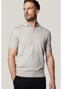 Jasnoszara koszulka polo z krótkim rękawem i kołnierzykiem w kształcie litery V, z prążkowanym dołem i gładką fakturą, zestawiona z ciemnymi spodniami. Brak widocznych logo lub wzorów.