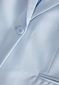 Helles blaues Jackenmaterial mit glatter Textur, ausgestattet mit einem einzelnen Knopf und einem Reverskragen-Design. Enthält ein dezentes, passendes Piping-Detail.