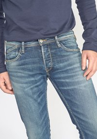 Lichtblauwe denim jeans met een vervaagde was, vijf zakken ontwerp en contrasterende stiksels. Sluit nauw om de dijen aan en wordt smaller bij de enkels.