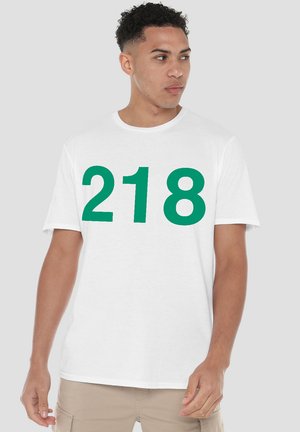 White cotton t-shirt featuring bold green text “218” on the front. Short sleeves and a crew neckline. Casual fit, minimal design.