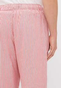 Punane ja valge triibuline pükste elastne vöökoht. Kangas tundub kerge ja sujuva tekstuuriga. Käsi on asetatud õmblusele lähemale.