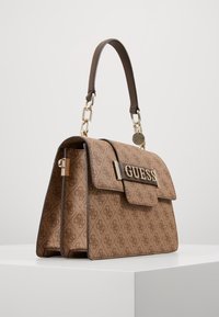 Ruskea kuvioitu käsilaukku, jossa on jämäkkä muotoilu, kullanväriset metalliosat, ketjutyylinen koriste ja läppä, jossa on keskellä logo.