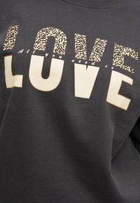 Μαύρο φούτερ με "LOVE" μπροστά· το επάνω μισό των γραμμάτων είναι σε λεοπάρ σχέδιο, το κάτω μισό σε μπεζ με χρυσό περίγραμμα. Μικρό κείμενο γράφει "All you need is".