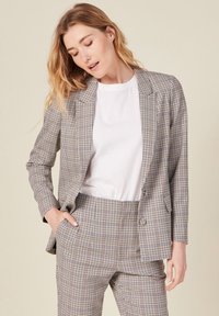 Ruudullinen bleiseri ja siihen sopivat housut neutraaleissa sävyissä, joissa on sileä rakenne, yhden nappivarren sulku ja klassiset viistot kaulukset.