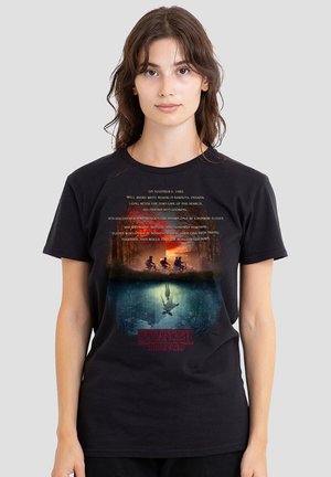 Schwarzes T-Shirt mit kurzen Ärmeln, das eine bedruckte Grafik mit Text und Bildern aus "Stranger Things" zeigt, einschließlich Charakteren und einer Waldszene.