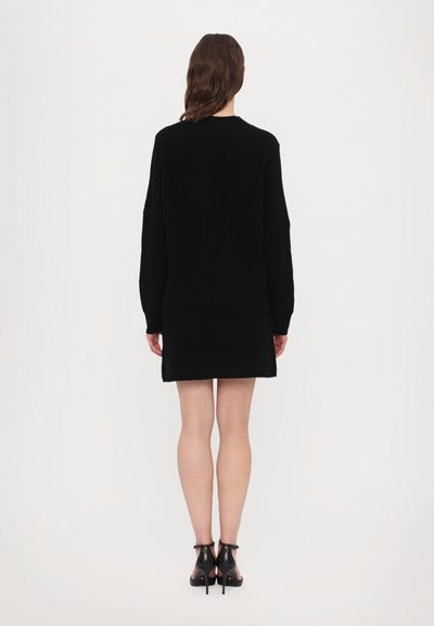 Maglione nero a maglia abbinato a una gonna nera, con taglio dritto e maniche lunghe. Indossato con tacchi aperti neri.