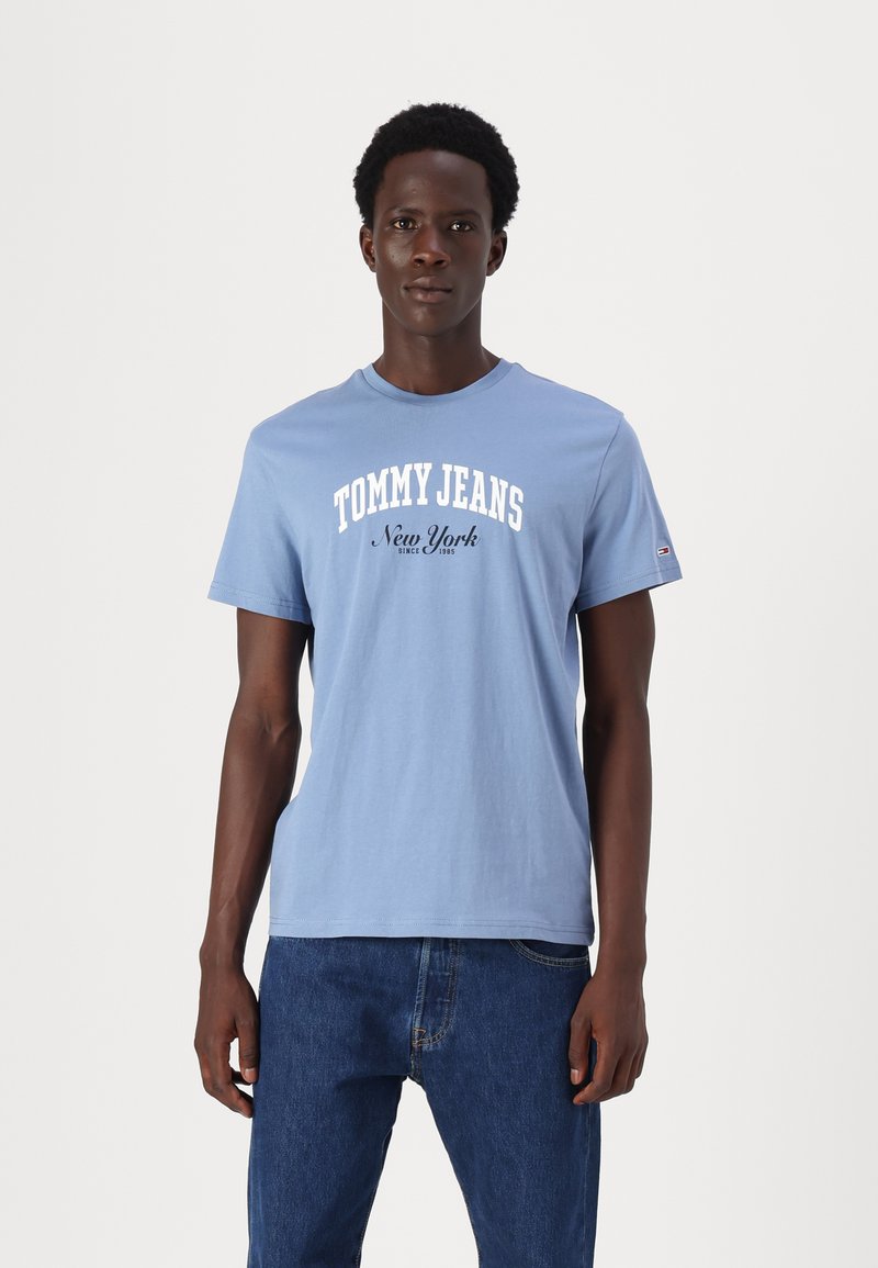 Gaiši zila kokvilnas T-krekla ar īsām piedurknēm, uz kura krūtīm ir uzraksts "TOMMY JEANS New York" baltā krāsā. Standarta izmērs, apaļa kakla izgriezums.