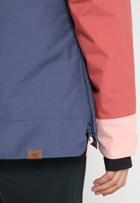 Kurtka wodoodporna w designie z blokami kolorów: granatowym, koralowym i różowym. Posiada boczną kieszeń na zamek oraz skórzaną metkę na dolnym końcu. Gładka faktura.