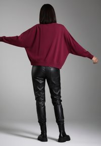 Maroon oversized sweater with wide sleeves, paired with black leather pants featuring a textured finish and elastic cuffs, worn with black boots.