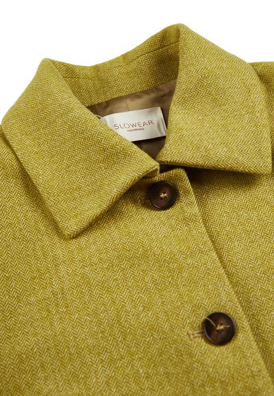 Cappotto a spina di pesce verde oliva con colletto classico, dotato di chiusura con bottone marrone e una consistenza morbida. Etichetta visibile all'interno.