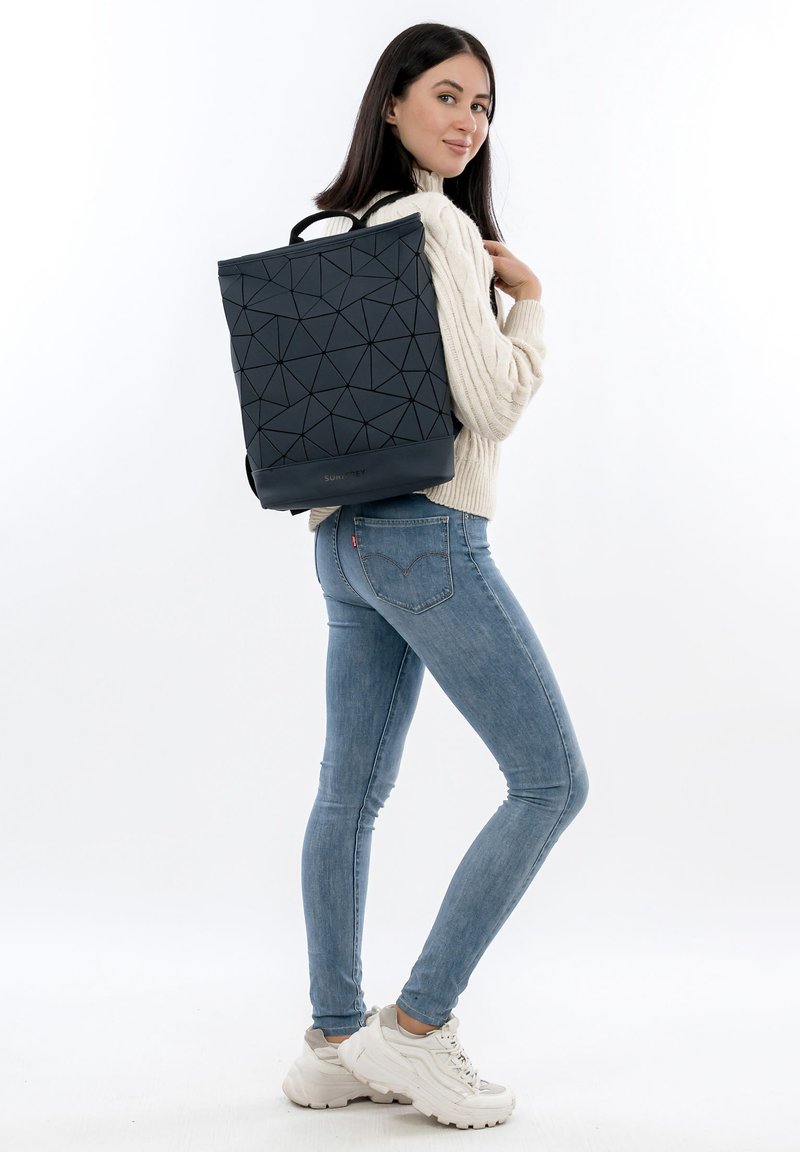 Svart ryggsäck med geometriskt mönster och texturerad yta samt ett handtag upptill, bärs på ryggen. Har justerbara remmar och robust design.