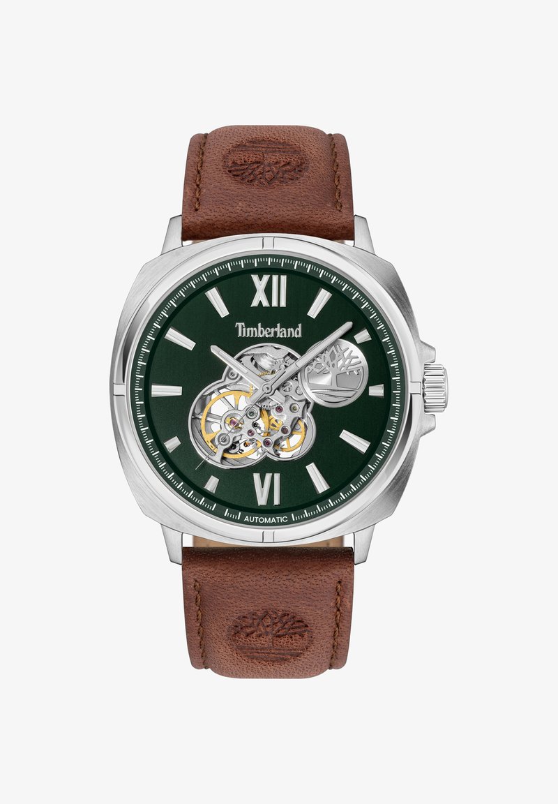 Montre automatique avec cadran vert foncé, boîtier argenté, bracelet en cuir marron et détail du mouvement apparent. Dispose de grands chiffres romains XII et VI.