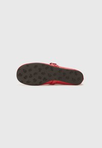 Red shoe sole with a textured black bottom featuring a floral pattern. The shoe has a smooth upper with straps and a buckle detail.